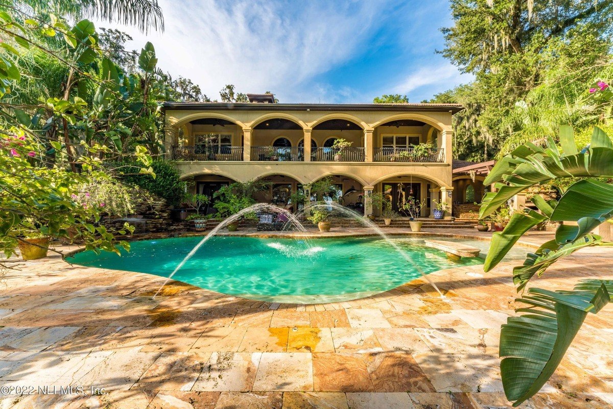 Large home has a swimming pool with fountain and lush landscaping.