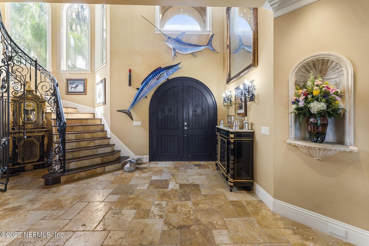 Grand entryway features a staircase, large dark doors, and mounted fish.