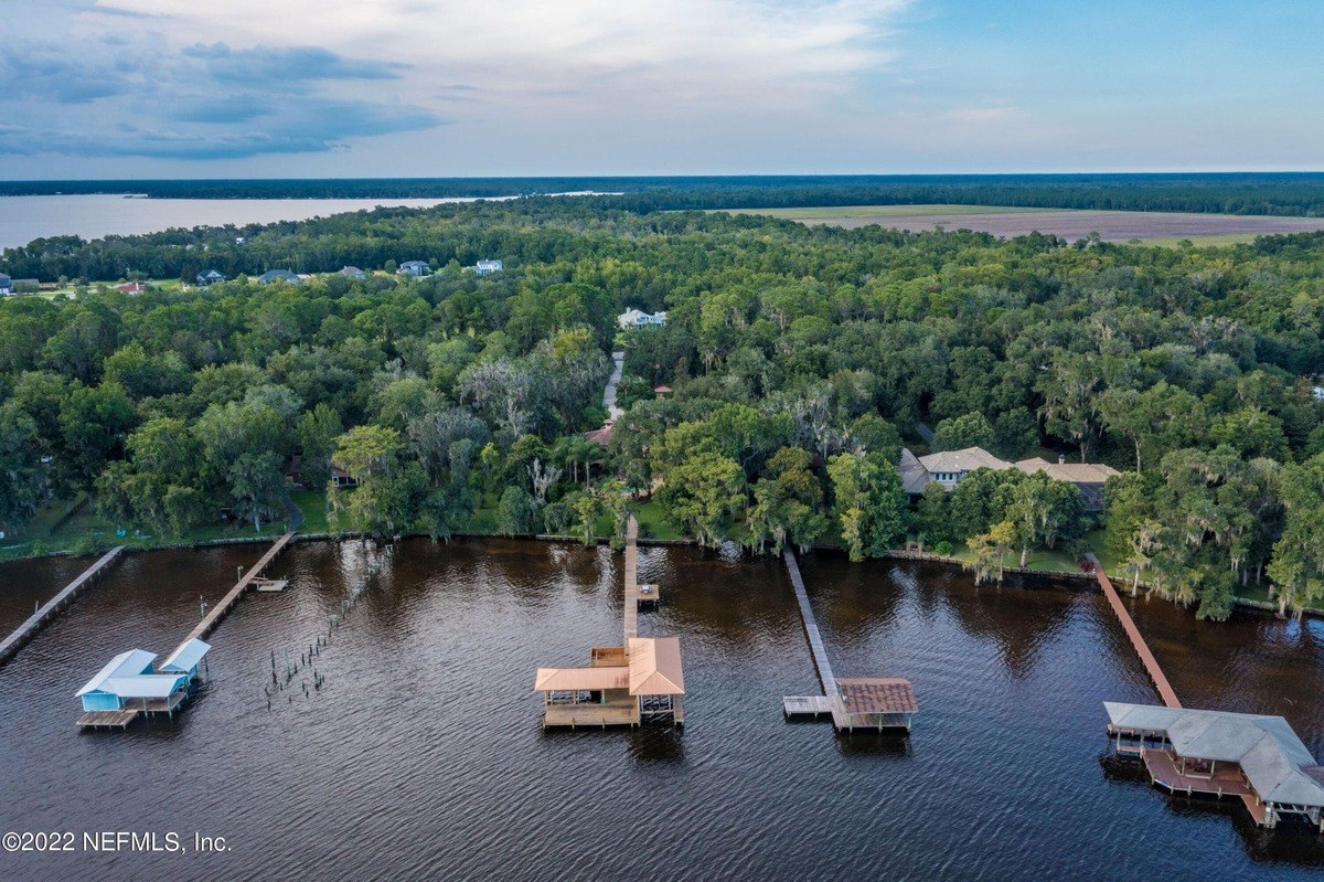 Aerial view shows waterfront property with multiple docks and houses surrounded by trees.