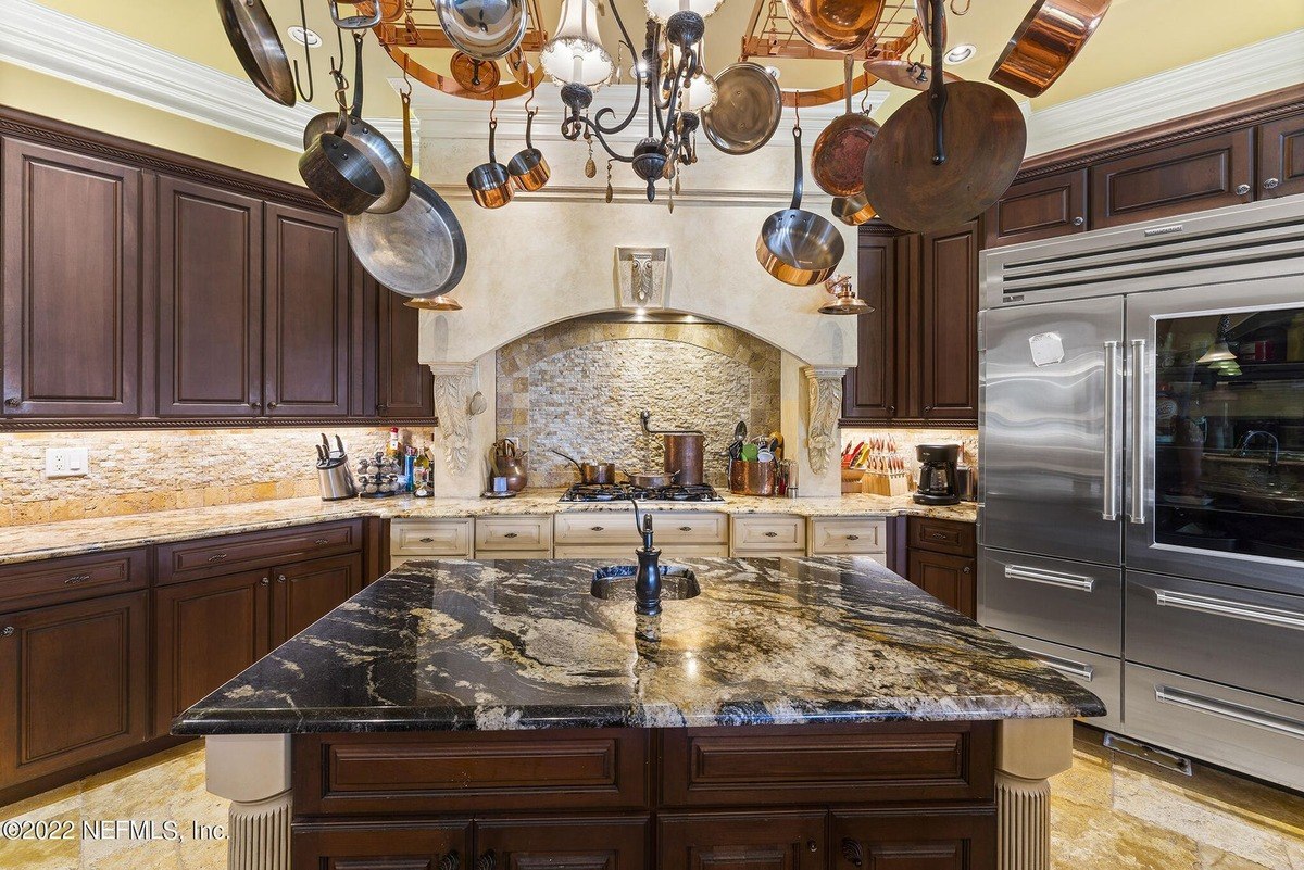 Kitchen features granite countertops, dark wood cabinets, and a pot rack hanging above the island.