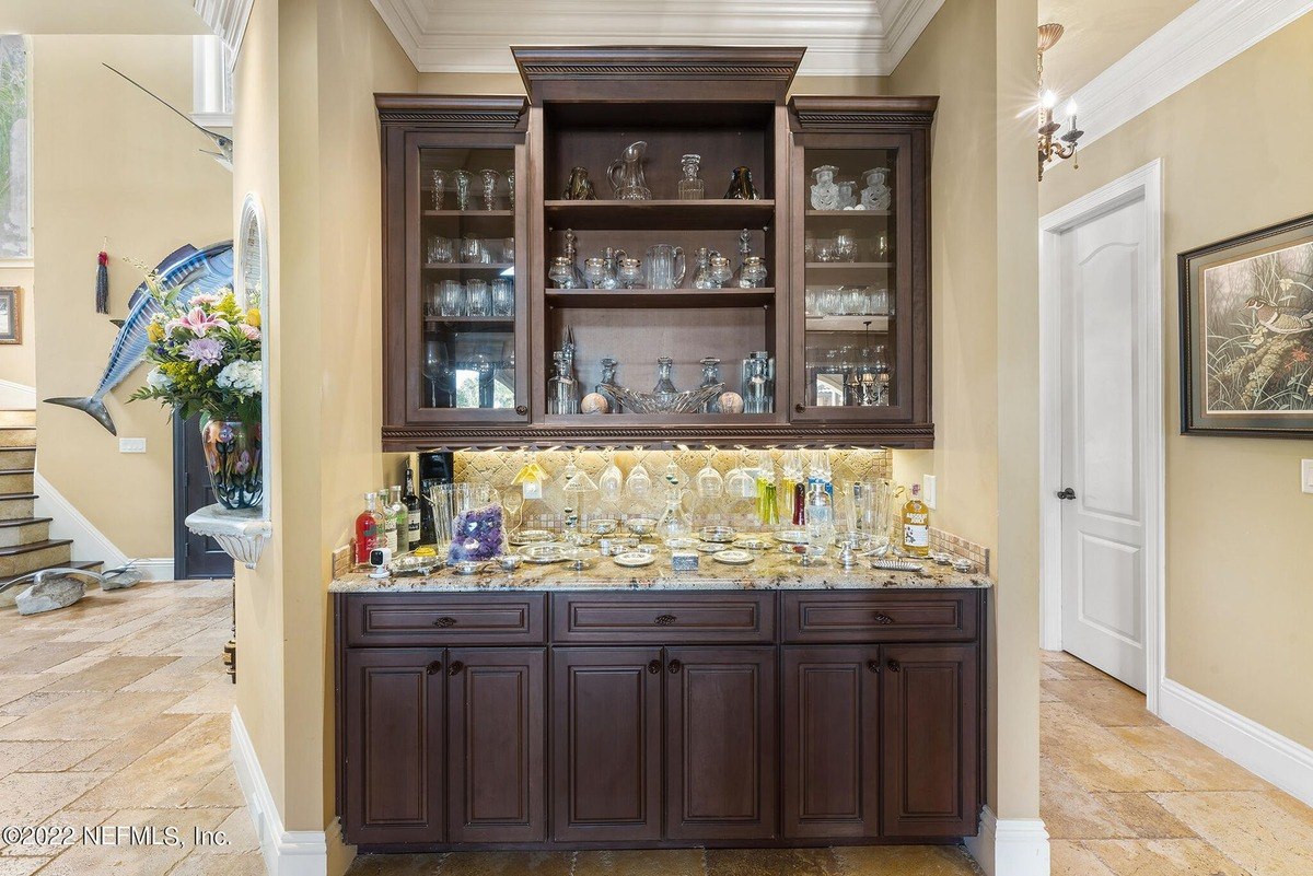 Built-in bar features glass-front cabinets, granite countertop, and various glassware.