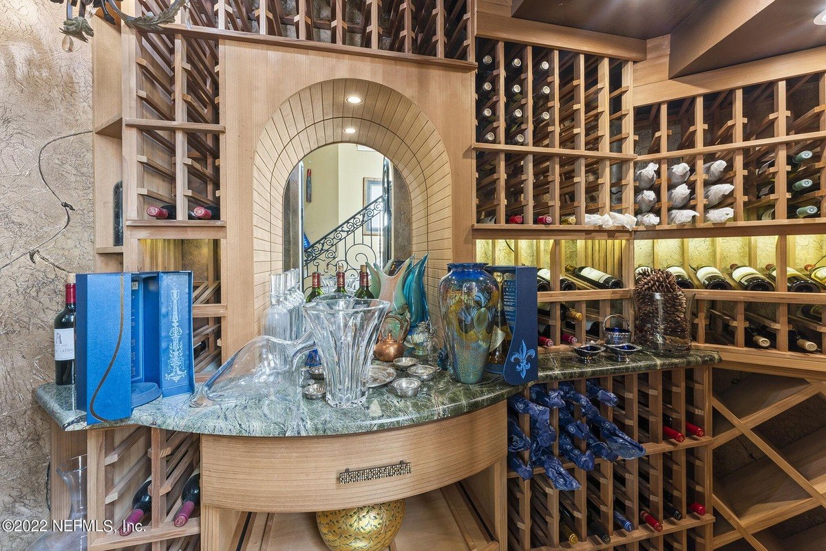 Wine cellar has wooden racks filled with wine bottles and a marble countertop with decorative items.