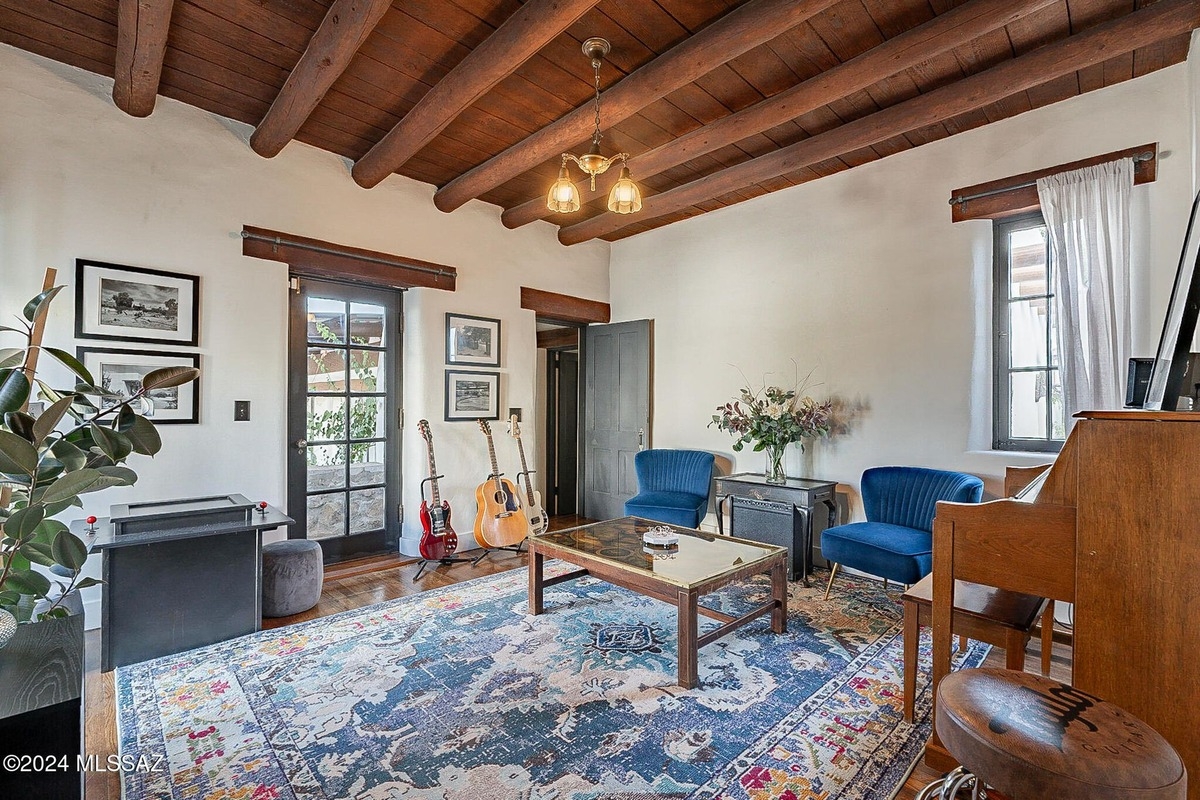 Room with wood beam ceiling, area rug, two blue chairs, coffee table, and guitars.