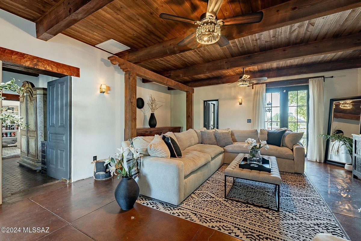 Living room with a large sectional sofa, wooden beams, and a patterned rug.