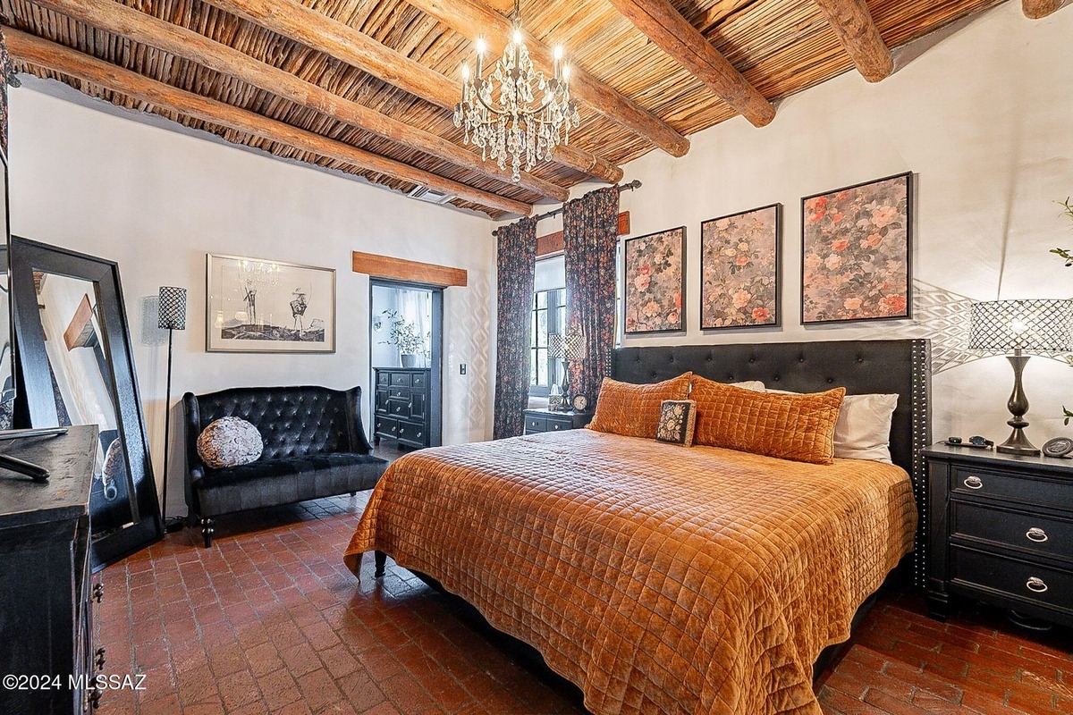 View of the bedroom highlights a tufted black bench, floral artwork, and elegant bedding.