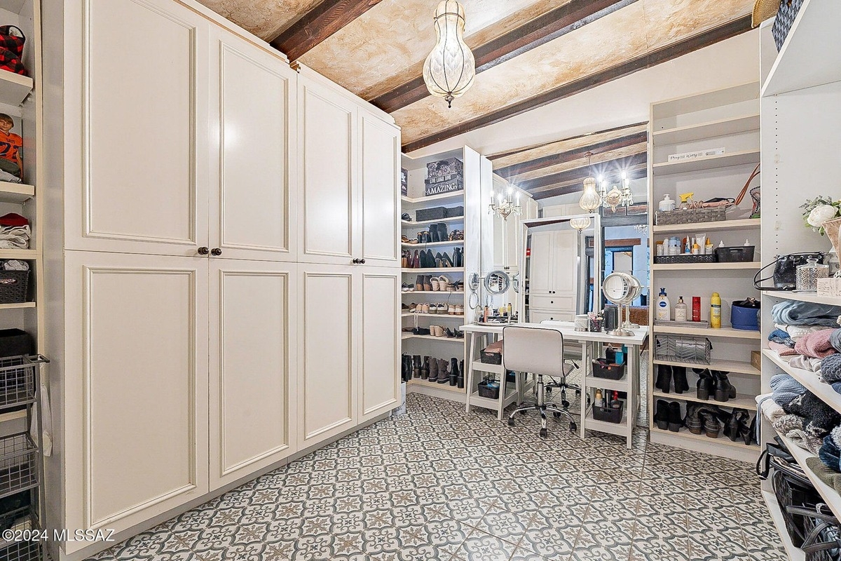 Large walk-in closet with white cabinets, open shelving, and a vanity area with a patterned floor. 