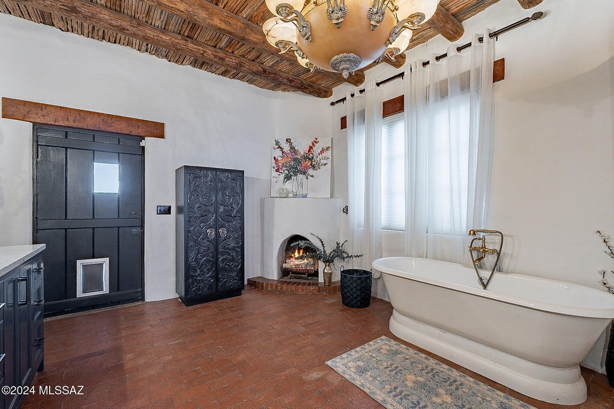 Rustic bathroom features a freestanding tub, fireplace, ornate wooden cabinet, and exposed wooden beams on the ceiling.