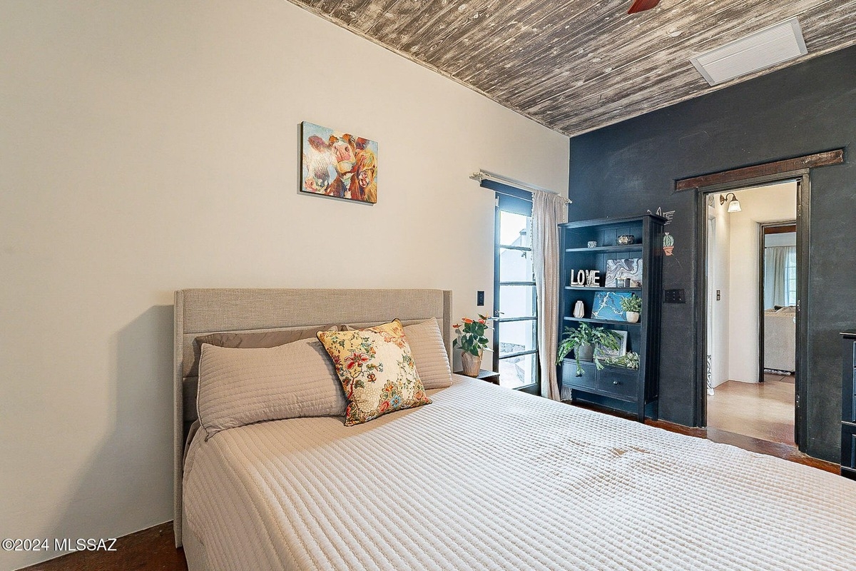 Bedroom with a bed, a bookcase, and a view of another room through an open doorway.