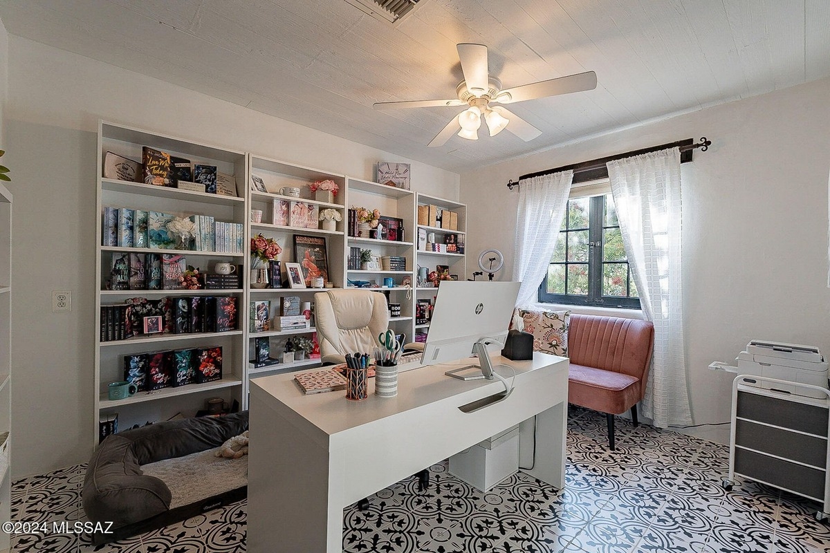 Home office with built-in bookshelves, a white desk, a pink chair, and a patterned floor.