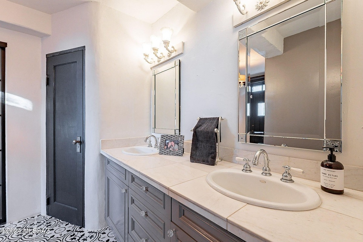 Bathroom features double sinks, gray cabinets, and black and white patterned floor tiles.