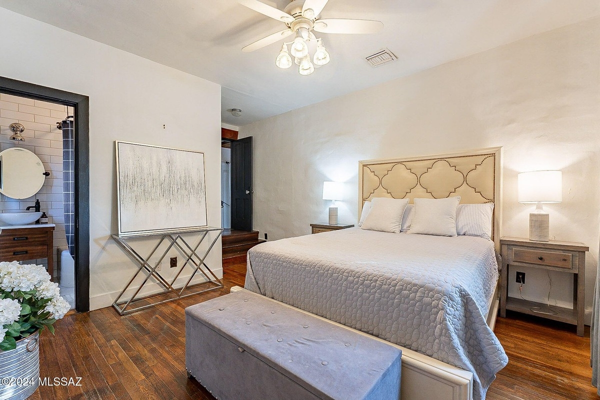 Bedroom with a bed, a ceiling fan, a piece of art, and a view of a bathroom.