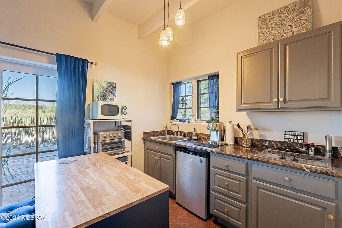 Small kitchen with gray cabinets, a wood countertop, and a view of a patio through a window. 