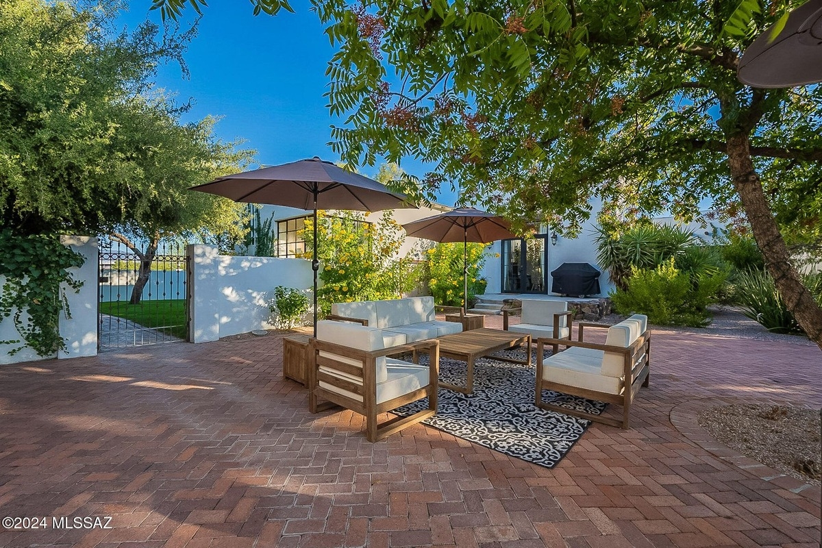 Outdoor patio furniture under umbrellas in a brick courtyard.