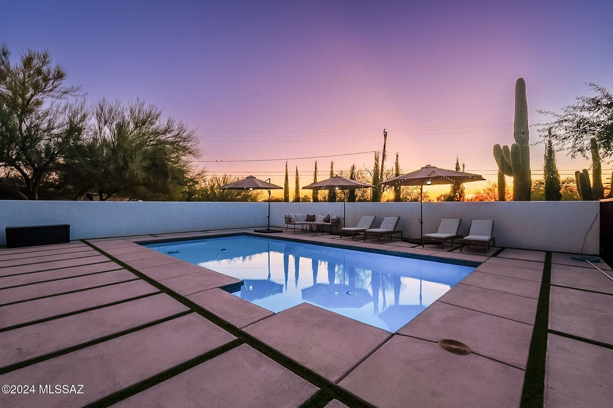 Rectangular swimming pool with lounge chairs and umbrellas at sunset.