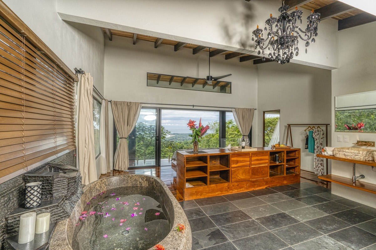 Bathroom has large stone bathtub, ocean view, and wood shelving.