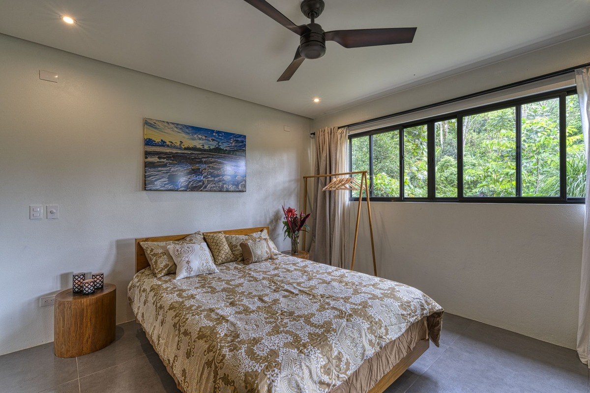 Bedroom has large bed, ceiling fan, and forest view.