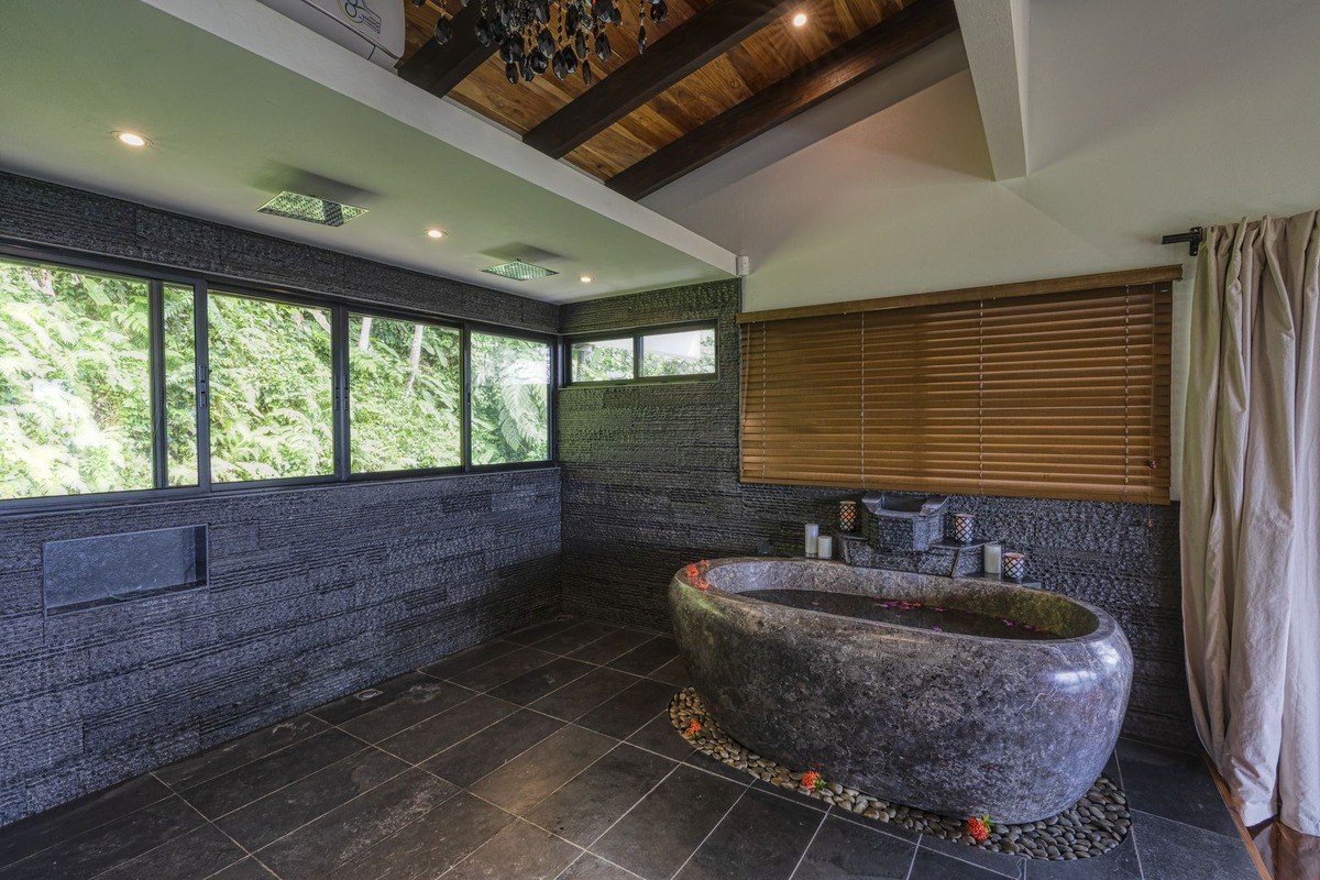 Bathroom has large stone bathtub, wood ceiling, and forest view.