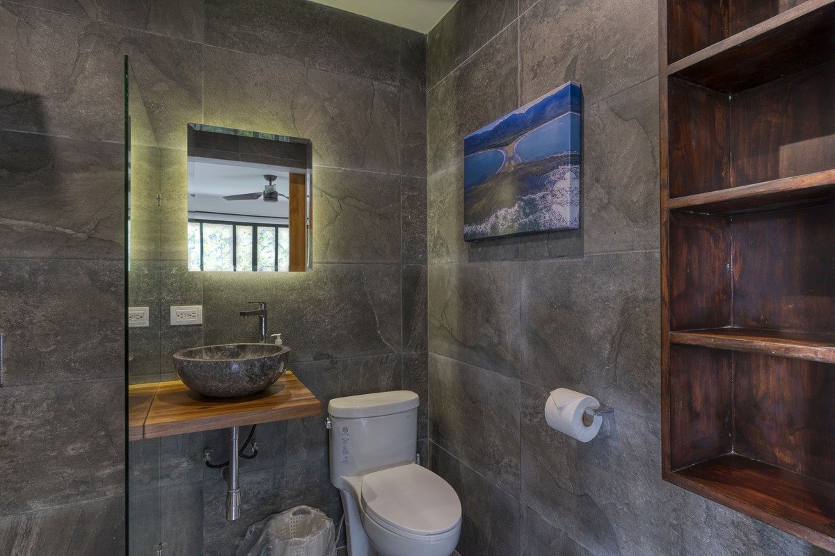 Bathroom has stone sink, toilet, and wood shelving.