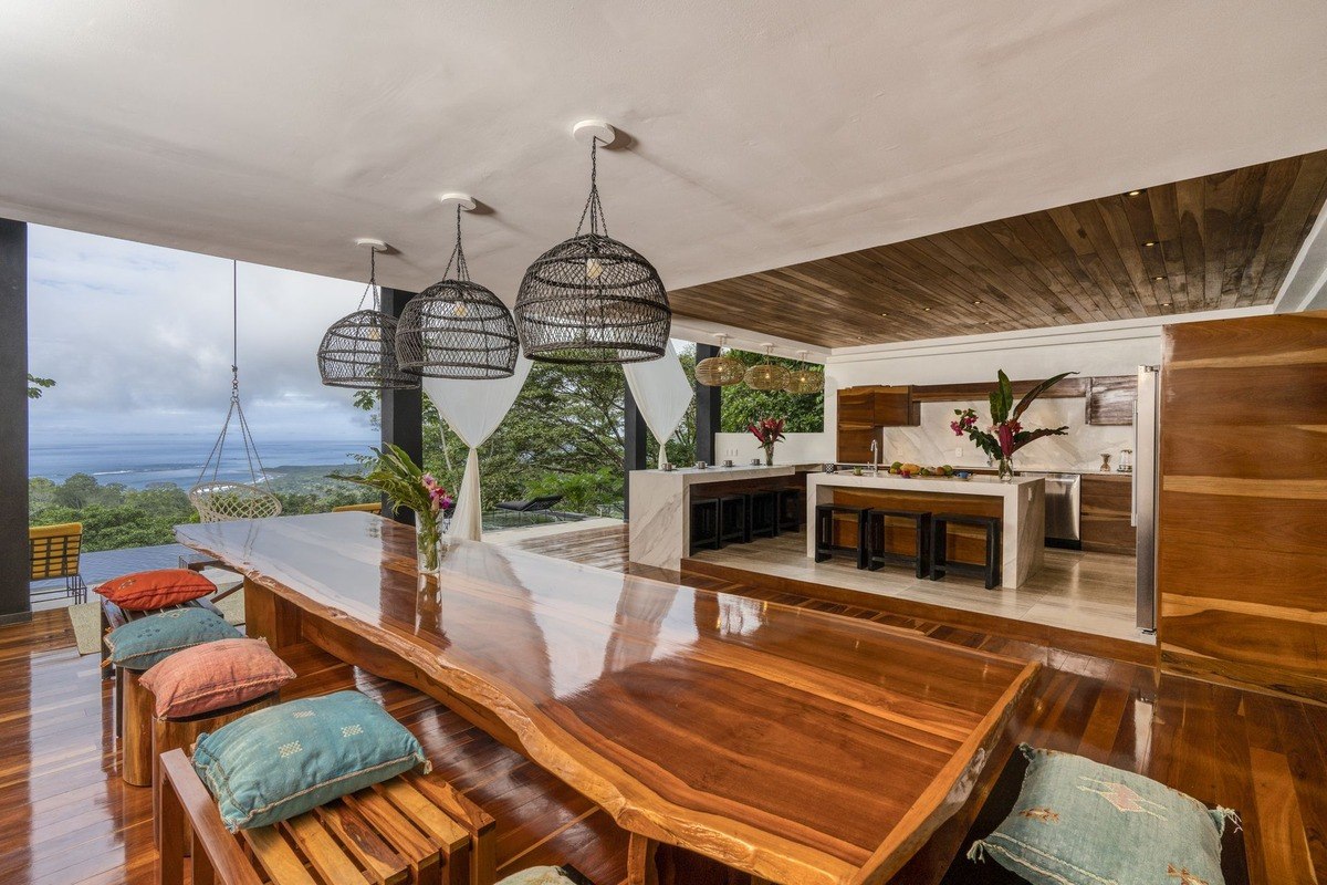 Dining area has large wood table, ocean view, and kitchen with island.