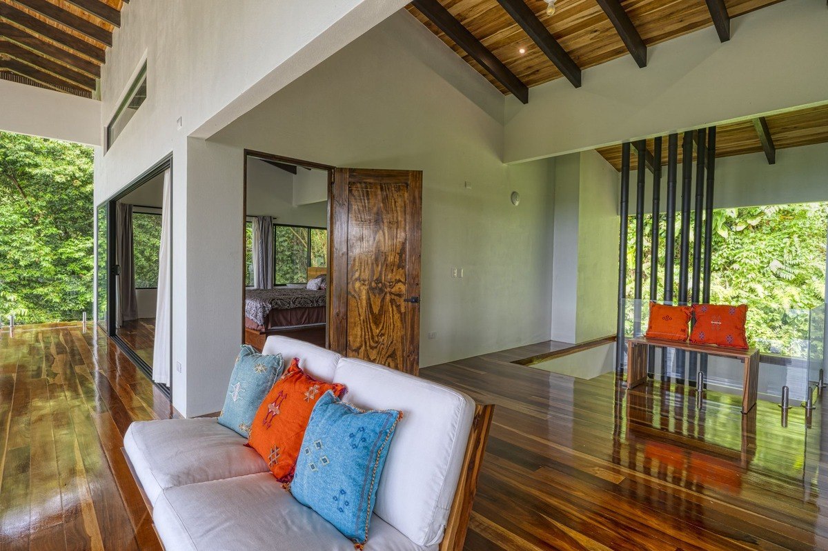 Living area has white couch, wood floors, and forest view.