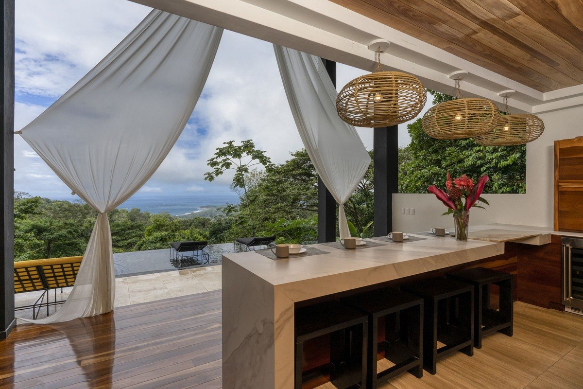 Kitchen has island with seating, ocean view, and woven light fixtures.