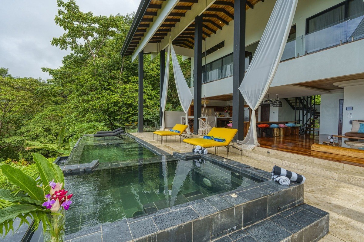 Infinity pool and hot tub are on patio with rainforest view.