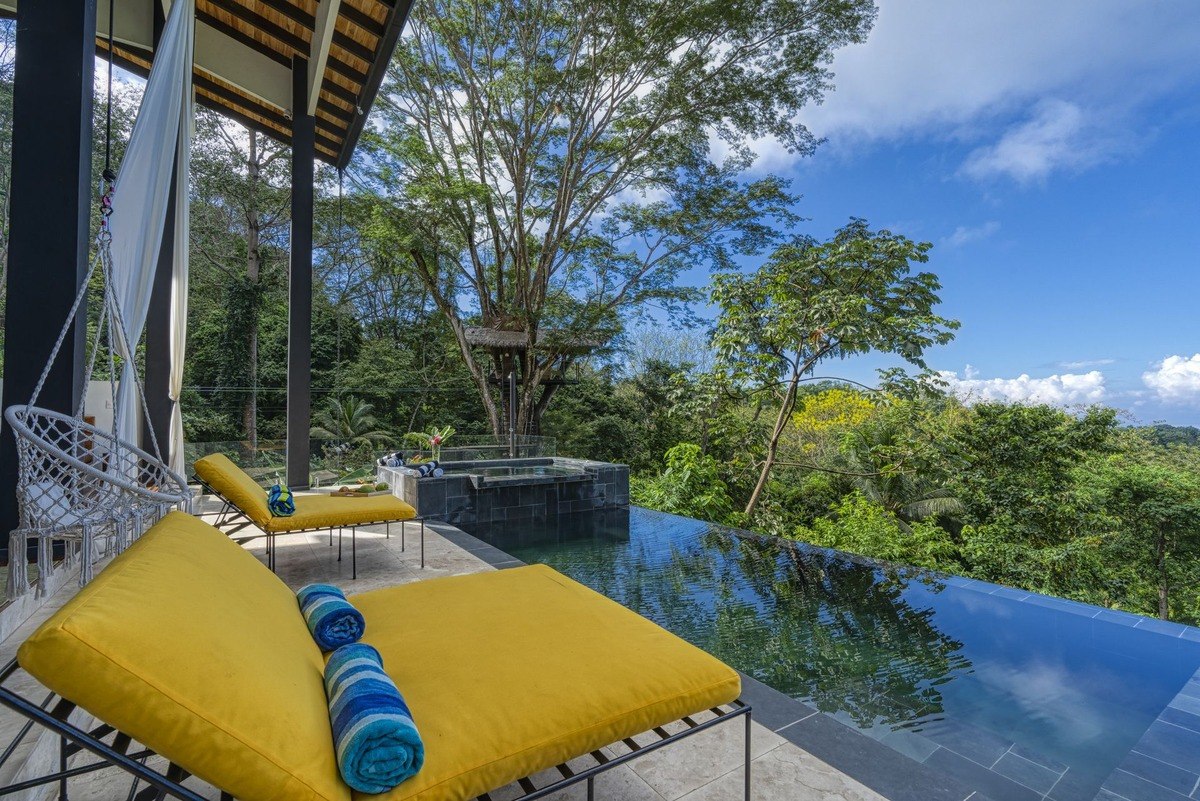 Infinity pool and hot tub are on patio with rainforest and treehouse views.