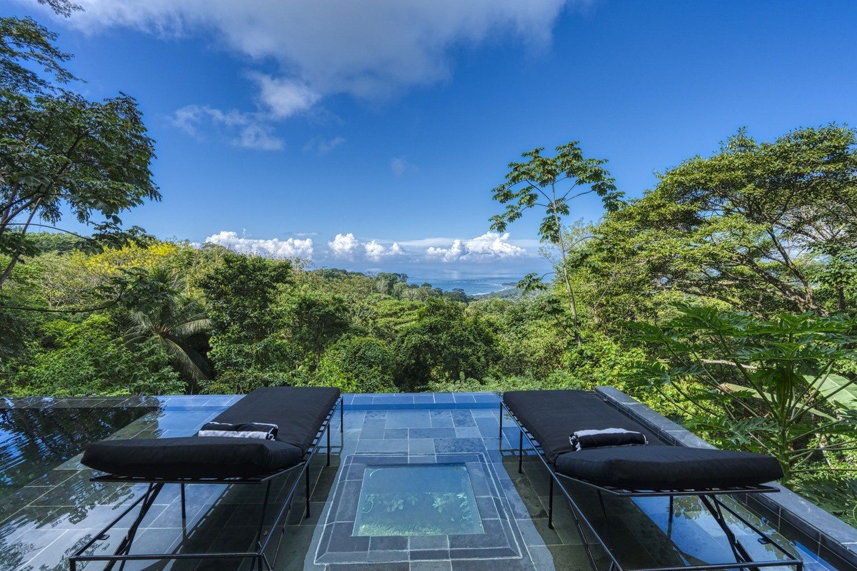 Pool and lounge chairs overlook rainforest and ocean.