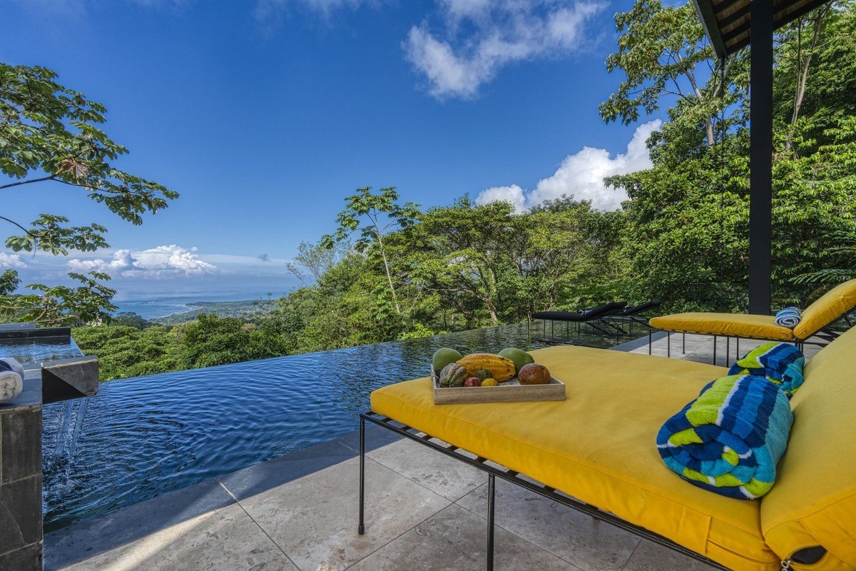 Infinity pool and lounge chairs overlook rainforest and ocean.