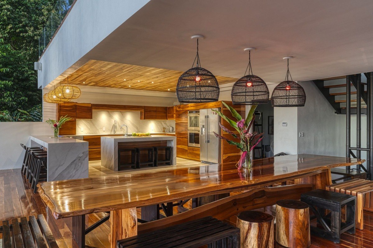 Dining area has large wood table, modern kitchen, and wood ceiling.