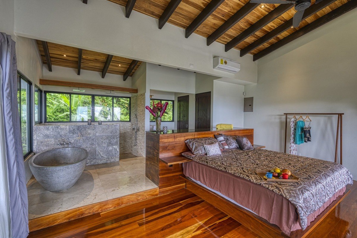 Bedroom has large bed, wood floors, and stone bathtub.