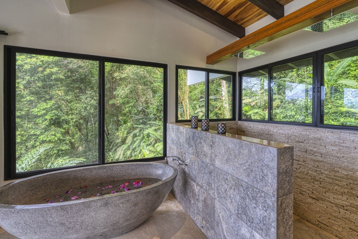 Bathroom has large stone bathtub and forest view.