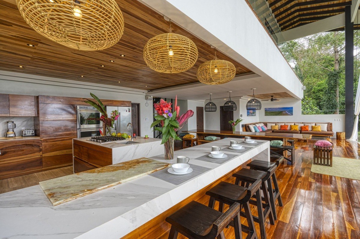 Kitchen has large island, wood cabinets, and woven light fixtures.