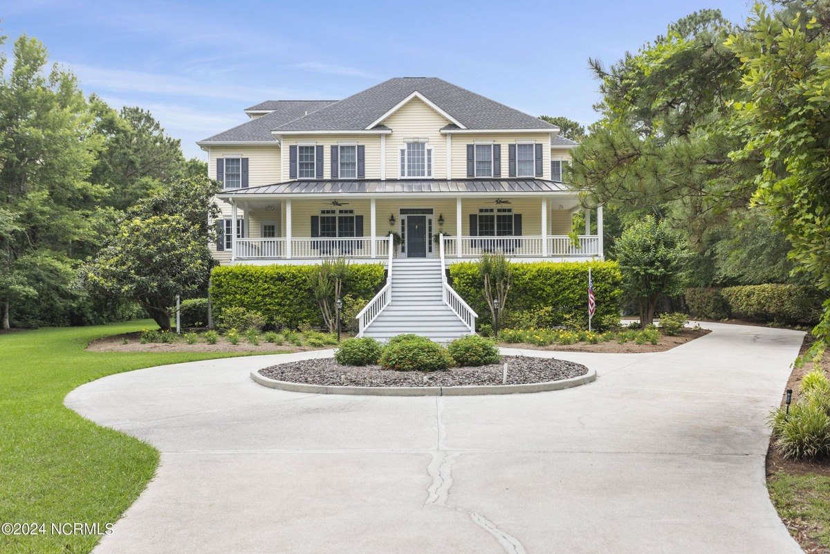 Large two-story house has a wraparound porch and a circular driveway.