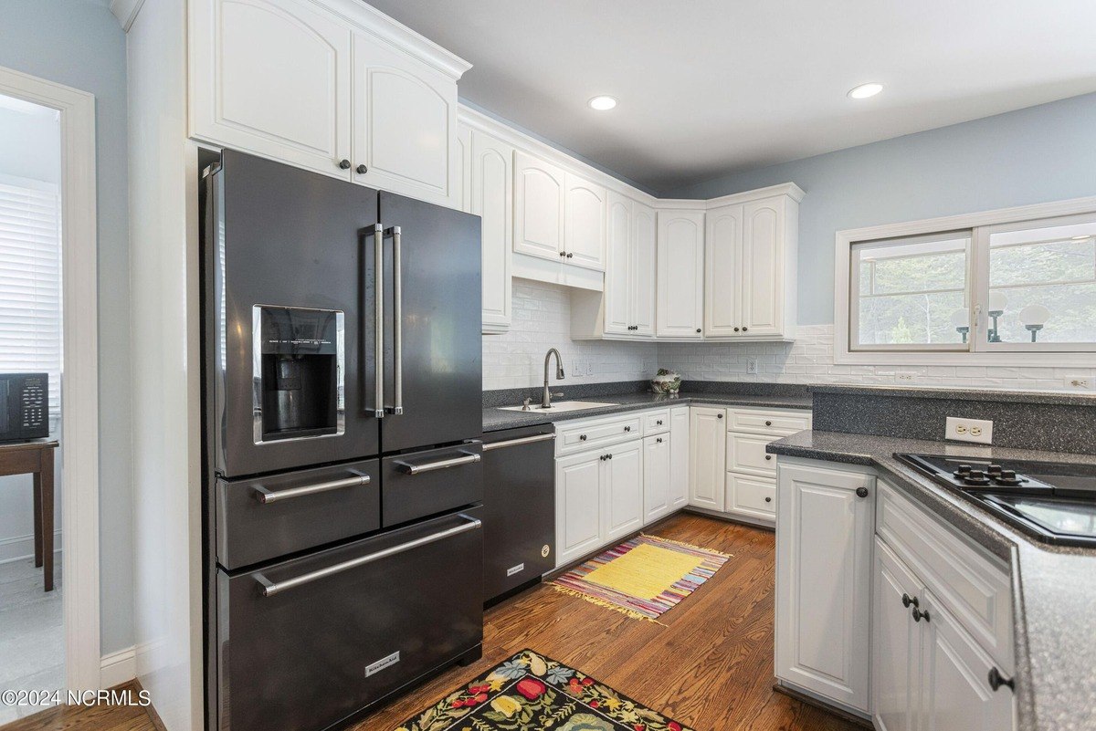 Kitchen has white cabinets, dark appliances, and granite countertops.