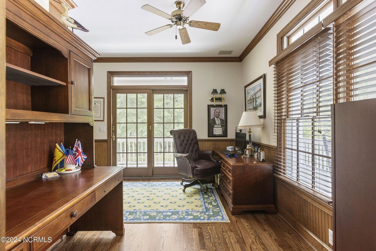 Home office has wood floors, a desk, and a leather chair.