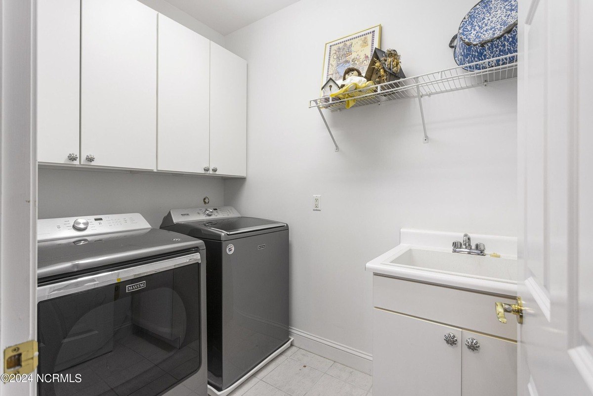 Laundry room has white cabinets, a sink, and gray washer and dryer.