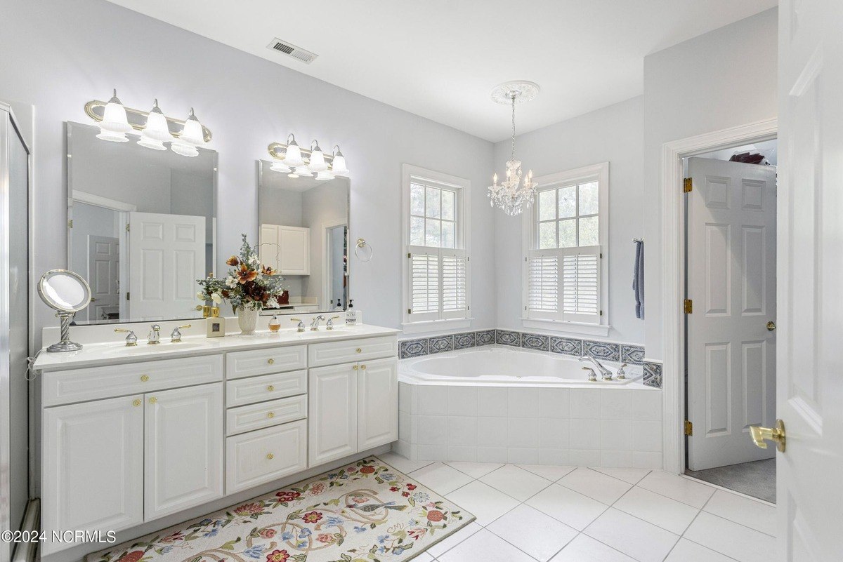 Bathroom has white cabinets, a corner tub, and double vanities.