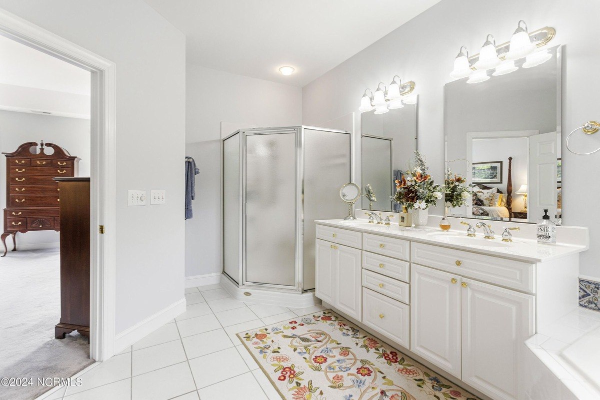 Bathroom has white cabinets, a shower, and double sinks.