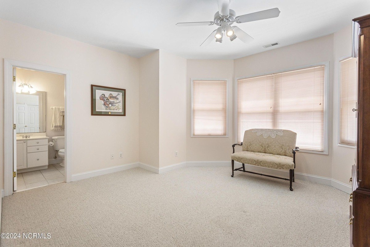 Bedroom has carpeted floors, a ceiling fan, and a small settee.