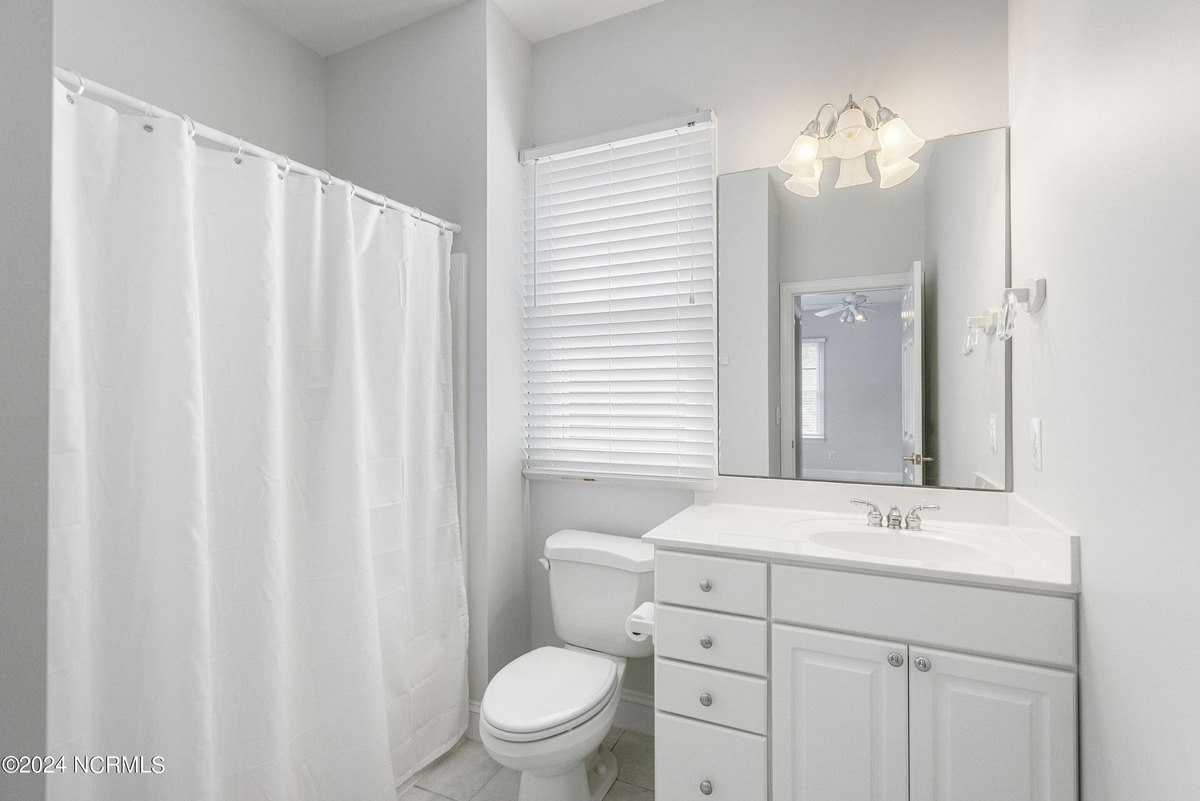 Bathroom has white cabinets, a toilet, and a shower with a white curtain.