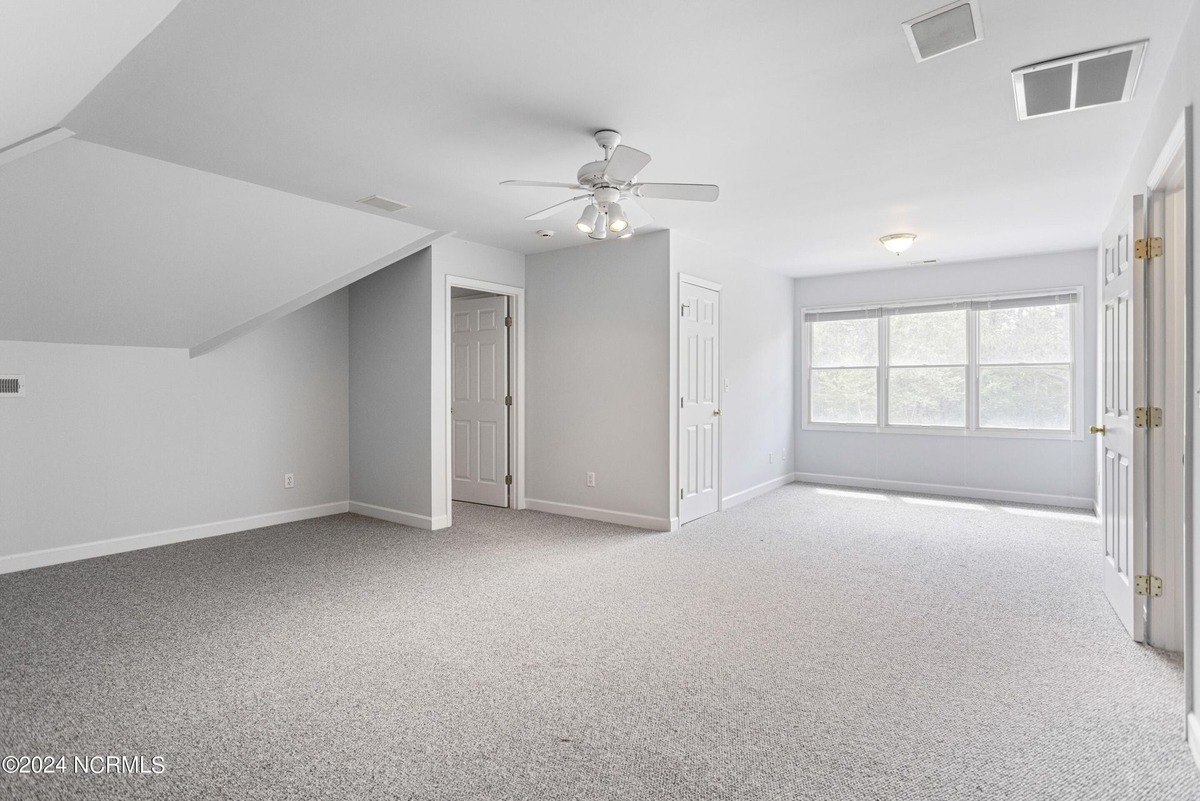 Large room has carpeted floors, a ceiling fan, and white walls.