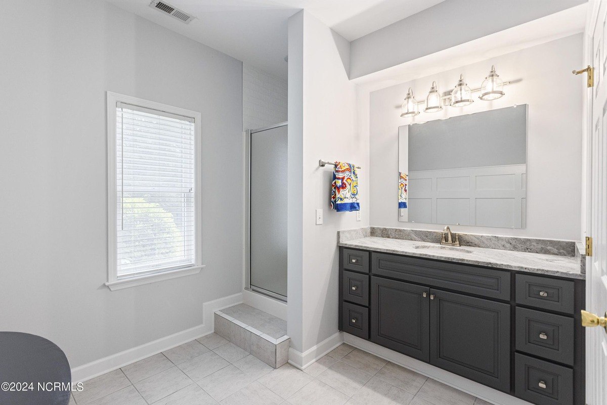 Bathroom has dark gray vanity, a shower, and a window with blinds.