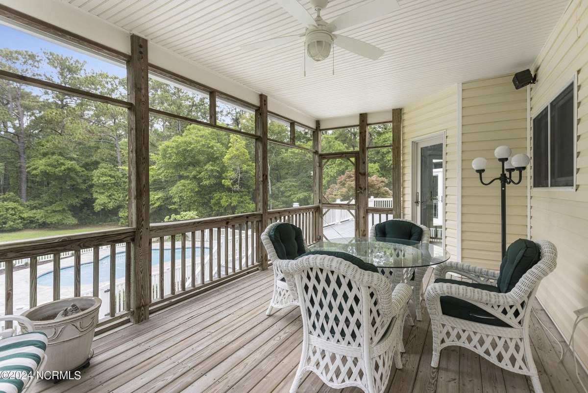 Screened porch has wicker furniture, a glass table, and a view of trees and a pool.