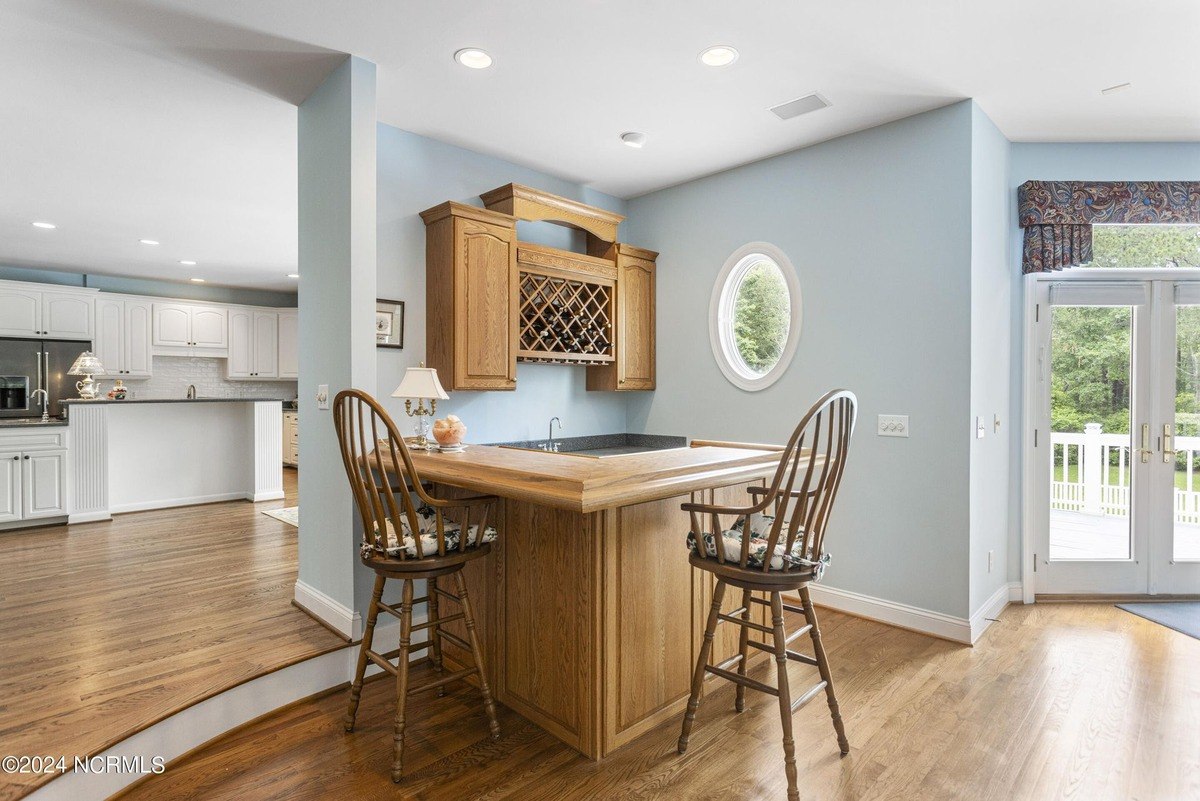 Home bar area has wood cabinets, a countertop, and two bar stools, with a view of a kitchen.