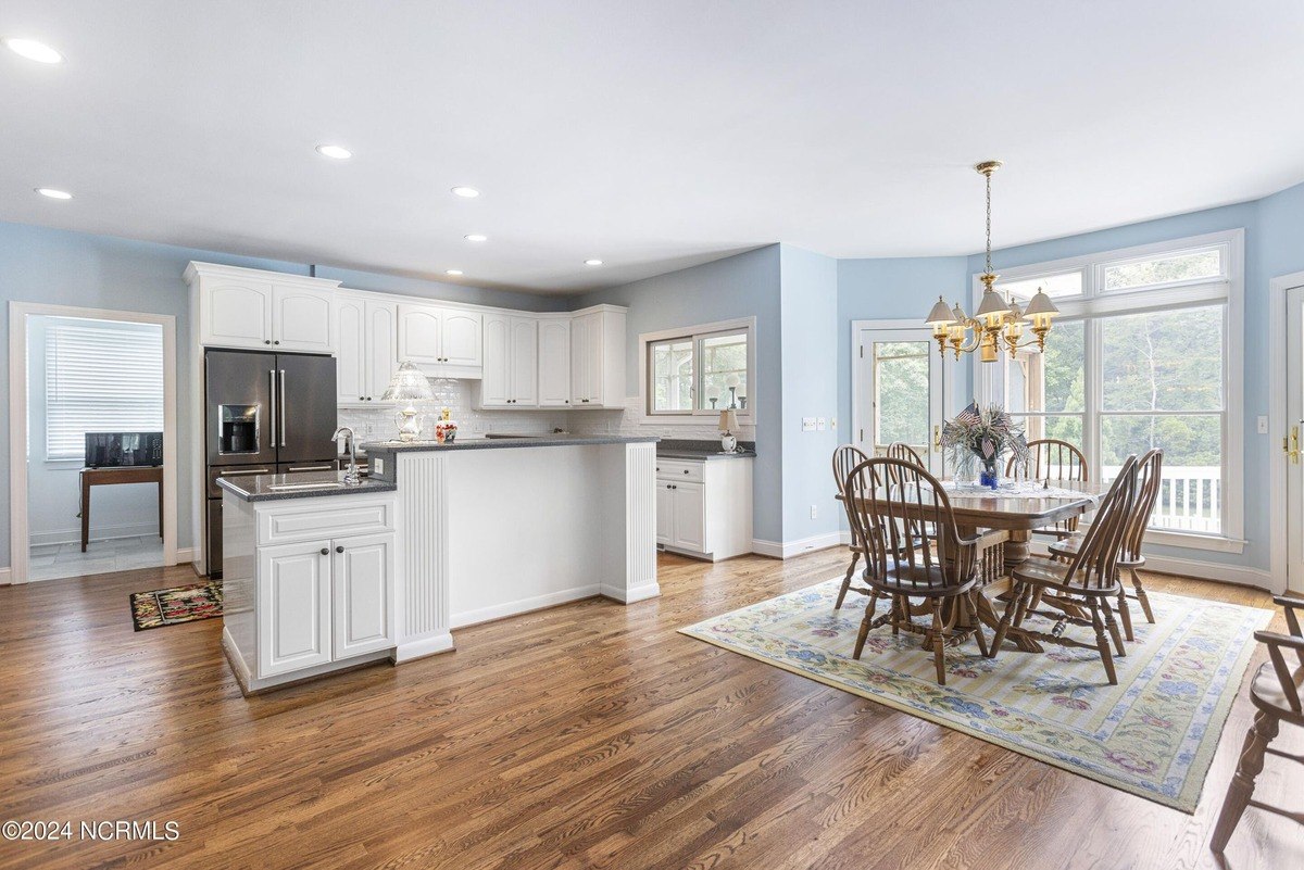 Kitchen and dining area have hardwood floors, white cabinets, and a large island.