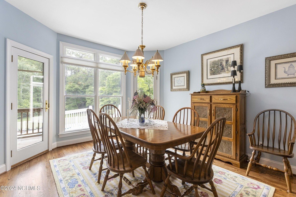 Dining room has hardwood floors, a wood table and chairs, and a view of trees.