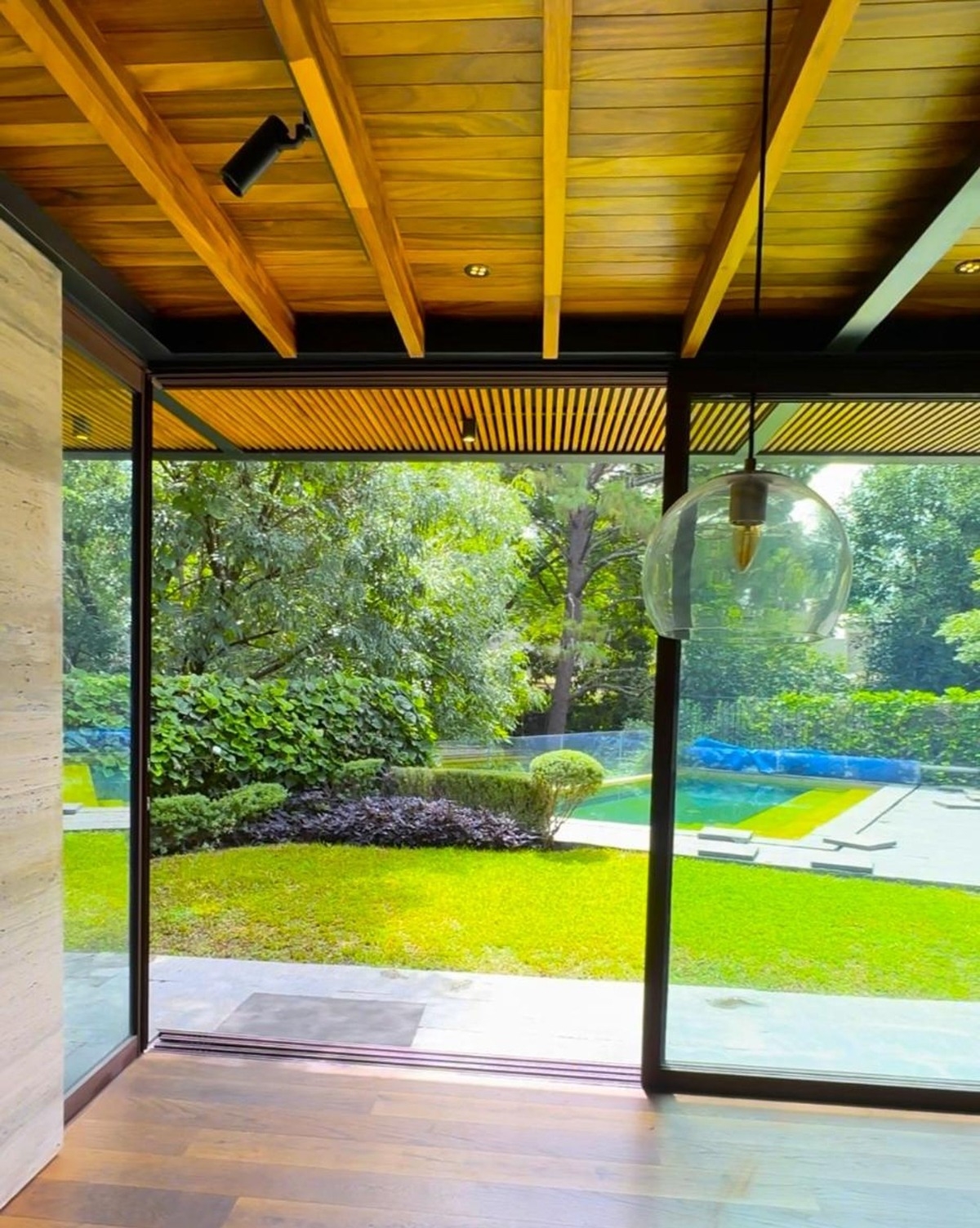 View of a lush green backyard through a large glass sliding door with a wooden ceiling above.