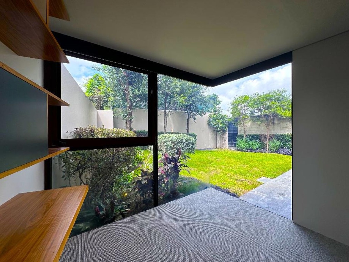 Bright green backyard framed by glass walls viewed from an indoor space with wooden shelves.