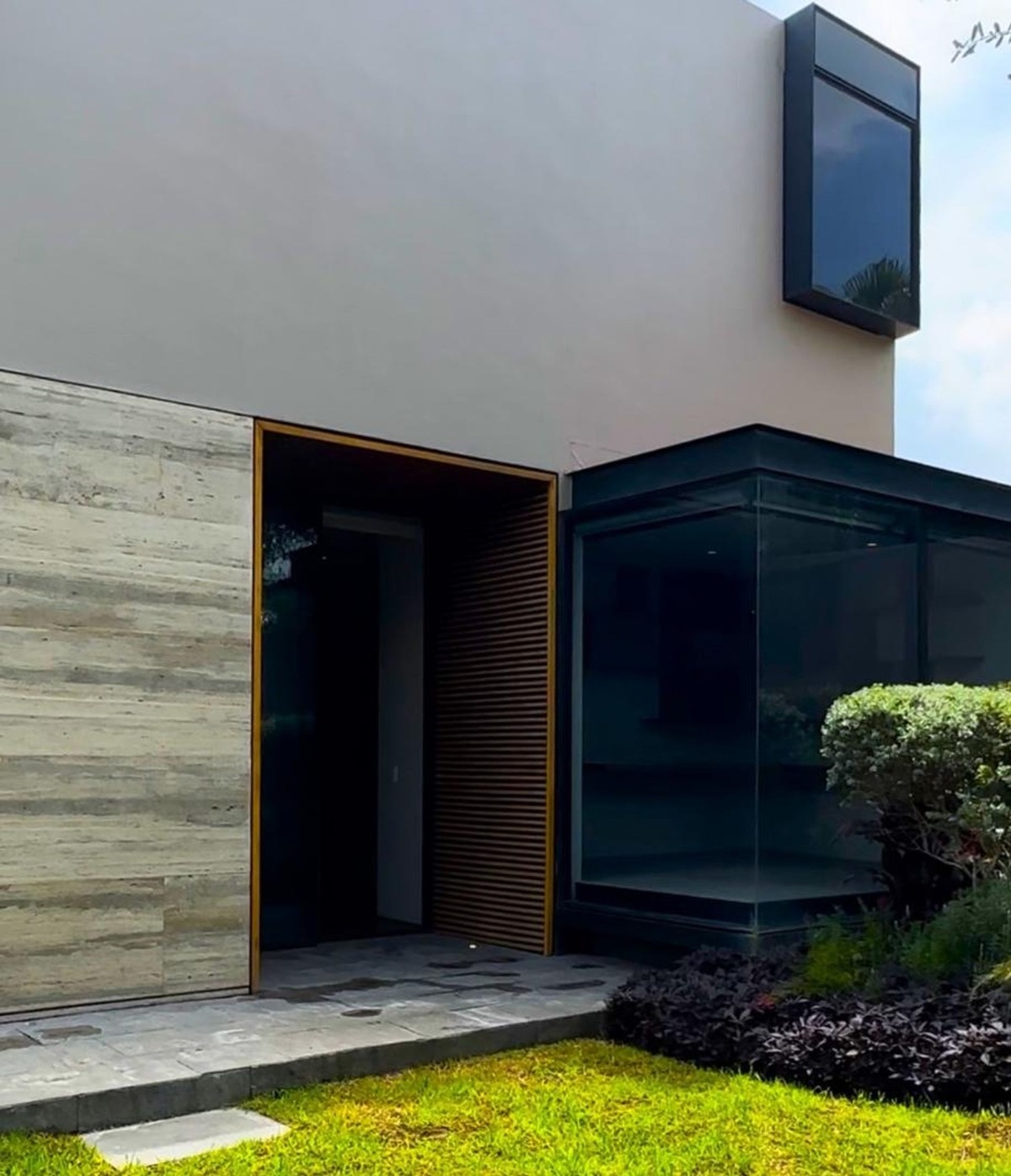 Modern facade with natural stone and glass elements bordered by landscaped greenery.